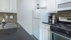 Una cucina con mobili bianchi, un piano di lavoro nero, un lavello in acciaio inossidabile, un frigorifero, una stufa e un forno a microonde.