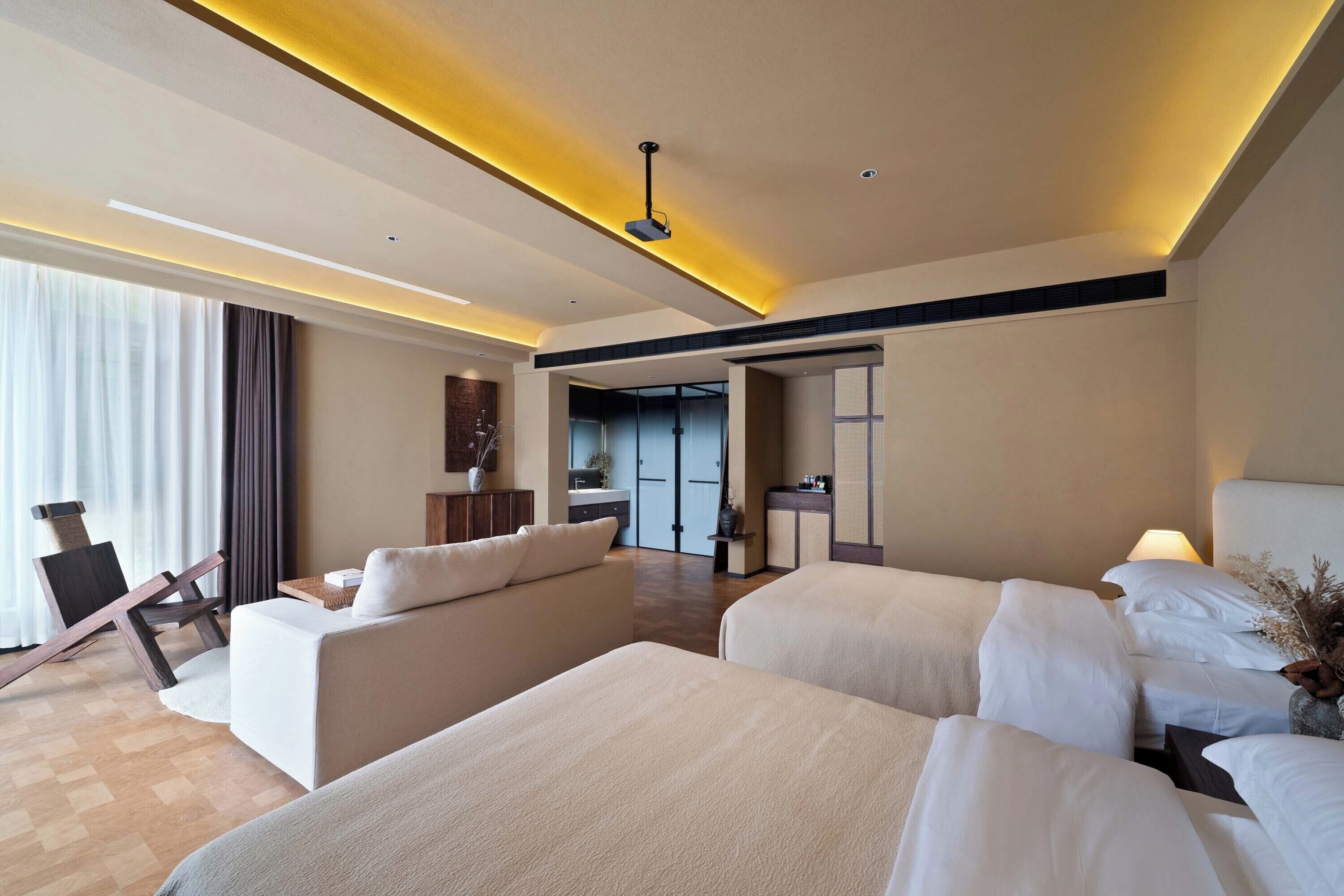 A modern hotel room with a large bed, a sofa, a desk, and a view of the hallway.