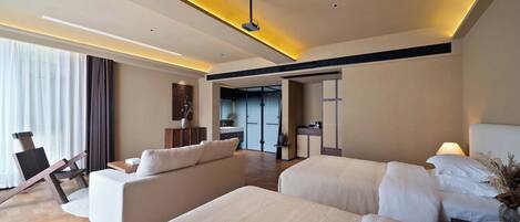 A modern hotel room with a large bed, a sofa, a desk, and a view of the hallway.