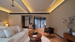 A modern living room with a white sofa, a wooden coffee table, and a black leather chair. There is a vase with dried plants on a wooden console table. - Fenghuang Border Town Mountain Homestay (Xiangxi)