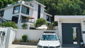 A modern two-story house with a white exterior, a car parked in the driveway, and a garage door. - Fenghuang Border Town Mountain Homestay (Xiangxi)