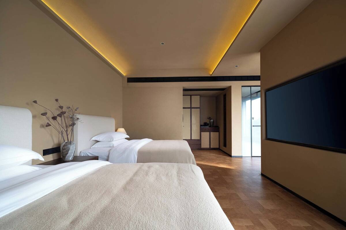 Een moderne hotelkamer met twee bedden, een grote flatscreen-tv en een minimalistisch design.