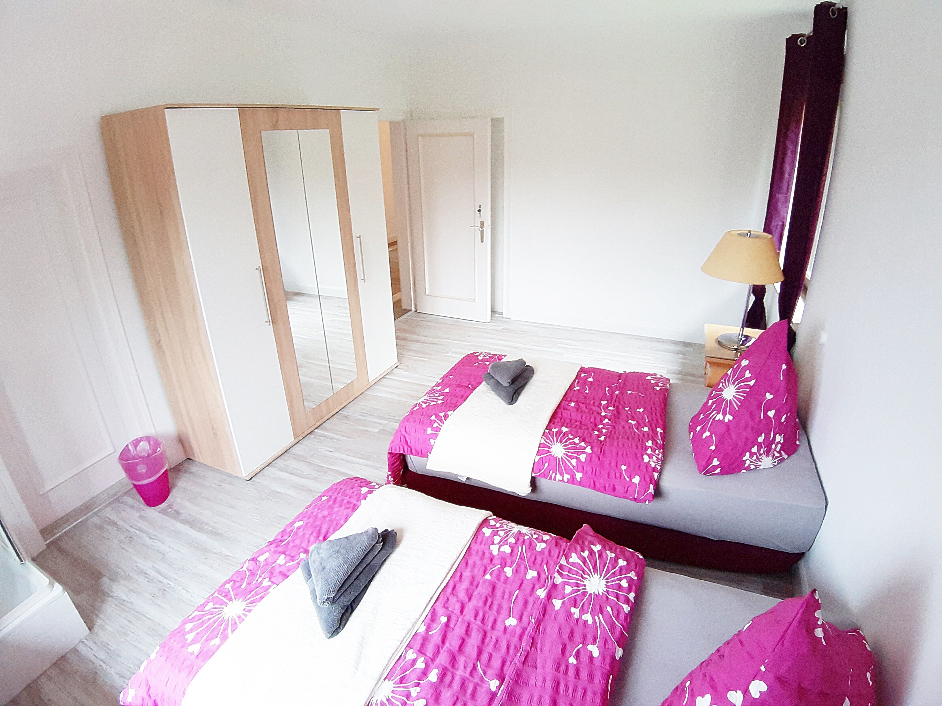 Une chambre avec deux lits, une armoire, un miroir et une lampe.