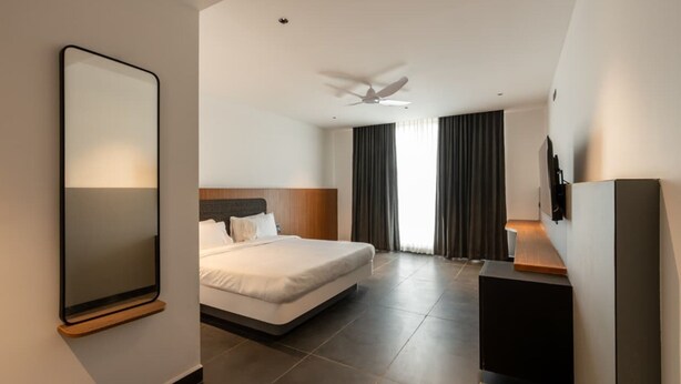Una habitación de hotel moderna con una cama grande, ventilador de techo, televisor de pantalla plana y un espejo amplio.