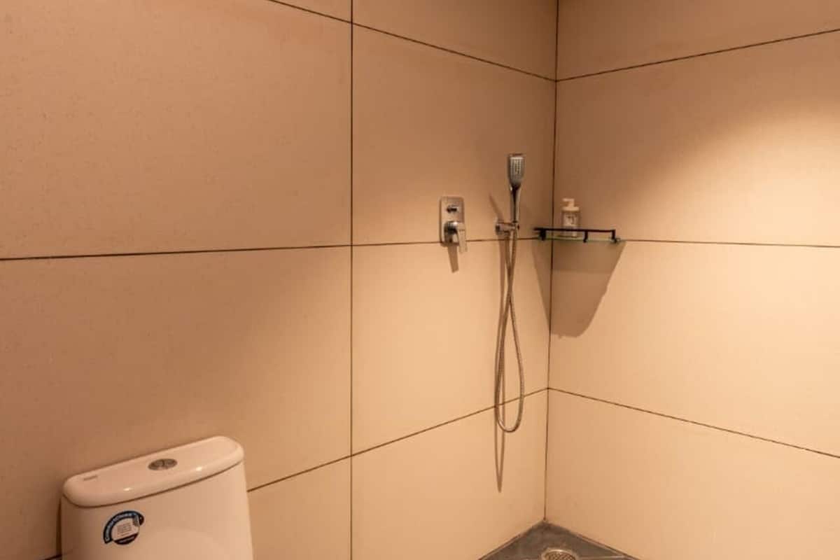 A small, modern bathroom with a toilet, a shower, and a shelf with toiletries.