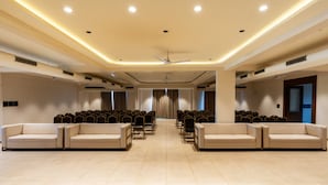 Una espaciosa sala de conferencias con filas de sillas, dos sofás, ventiladores de techo e iluminación empotrada.
