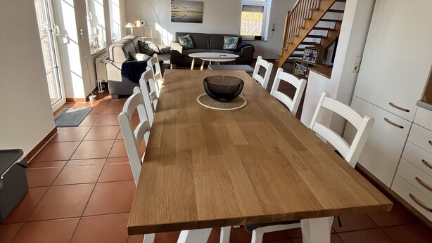 A spacious dining area with a long wooden table, white chairs, and a view of a kitchen and living area in the background. - Detached house for sole use - first floor exclusively for 2 people (Dornum)