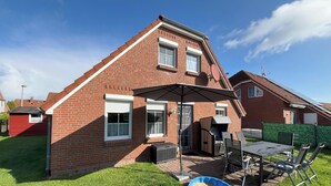 A two-story brick house with a patio area featuring a table and chairs, a barbecue grill, and a covered seating area. - Detached house for sole use - first floor exclusively for 2 people (Dornum)