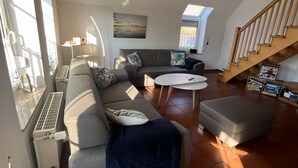 A living room with a sofa, ottoman, and a small table. There is a radiator, a window, and a staircase. - Detached house for sole use - first floor exclusively for 2 people (Dornum)