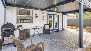 Un patio couvert aménagé avec des meubles en osier, un barbecue et une porte bleue.