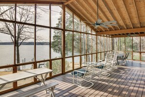 Eine überdachte Terrasse mit Holzboden, großen Fenstern und Sitzgelegenheiten im Freien.