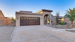 A residential house with a large garage, a covered driveway, and a landscaped garden with palm trees. - Private Pool, Spa! Updated Home Near London Bridge (Lake Havasu City)