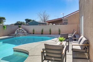 A swimming pool with a stone feature, outdoor seating, and a building in the background. - Stunning Renovated 5BR House w/Pool 7 mil to strip (Las Vegas)