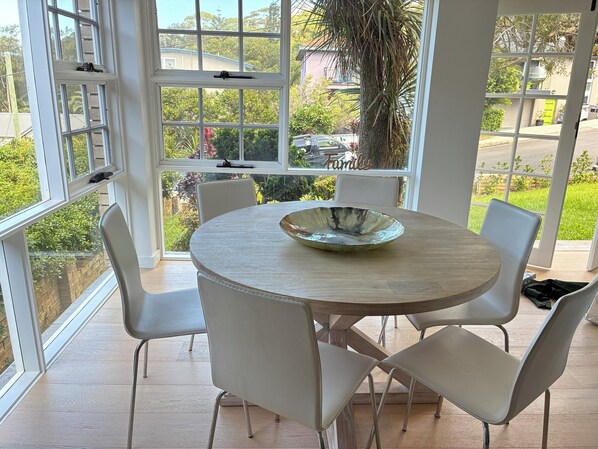 A dining area with a round table, white chairs, and a large window with a view of greenery and buildings.