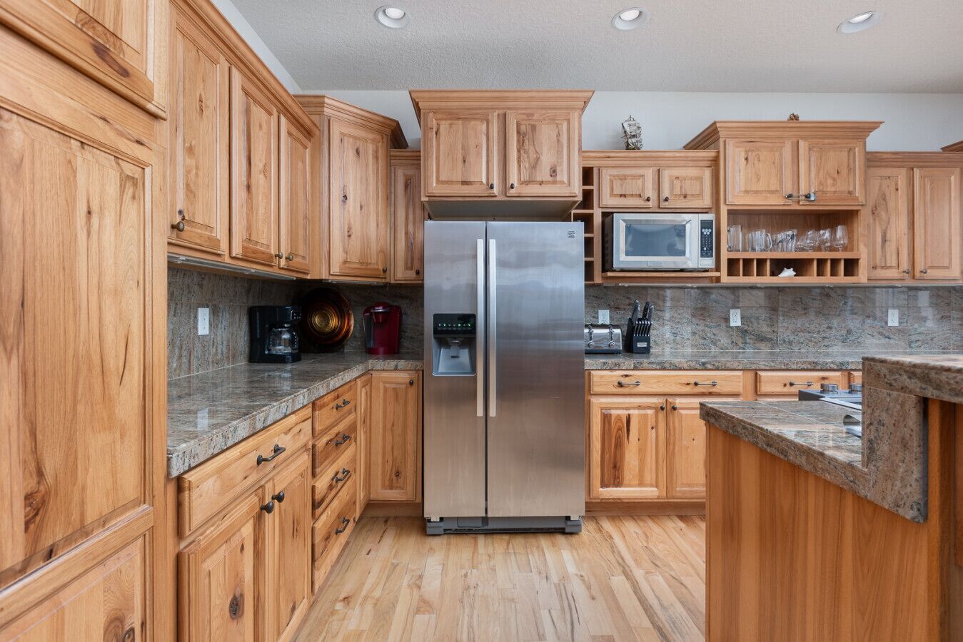 A kitchen with wooden cabinets, a stainless steel refrigerator, a microwave, and granite countertops.