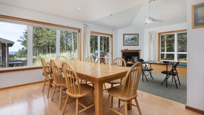 Un comedor amplio con una gran mesa de madera y sillas, una chimenea y ventanas grandes que ofrecen vistas al exterior.