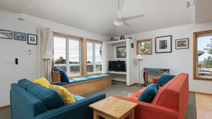 Una sala de estar moderna con un sofá azul, un sofá rojo y una mesa de centro de madera. Hay un televisor y una mesita con una lámpara.