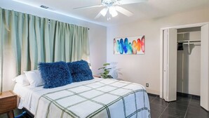 Ein Schlafzimmer mit Bett, Deckenventilator, grünem Vorhang und einem farbenfrohen Wandbild.