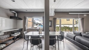 A modern kitchen with a built-in stove, a dining area with a table and chairs, and a living area with a sofa and large windows. - THE LAVENRIDGE (Nakafurano)