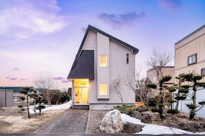 A modern two-story house with a sloped roof, a front entrance with glass doors, and a small porch area.