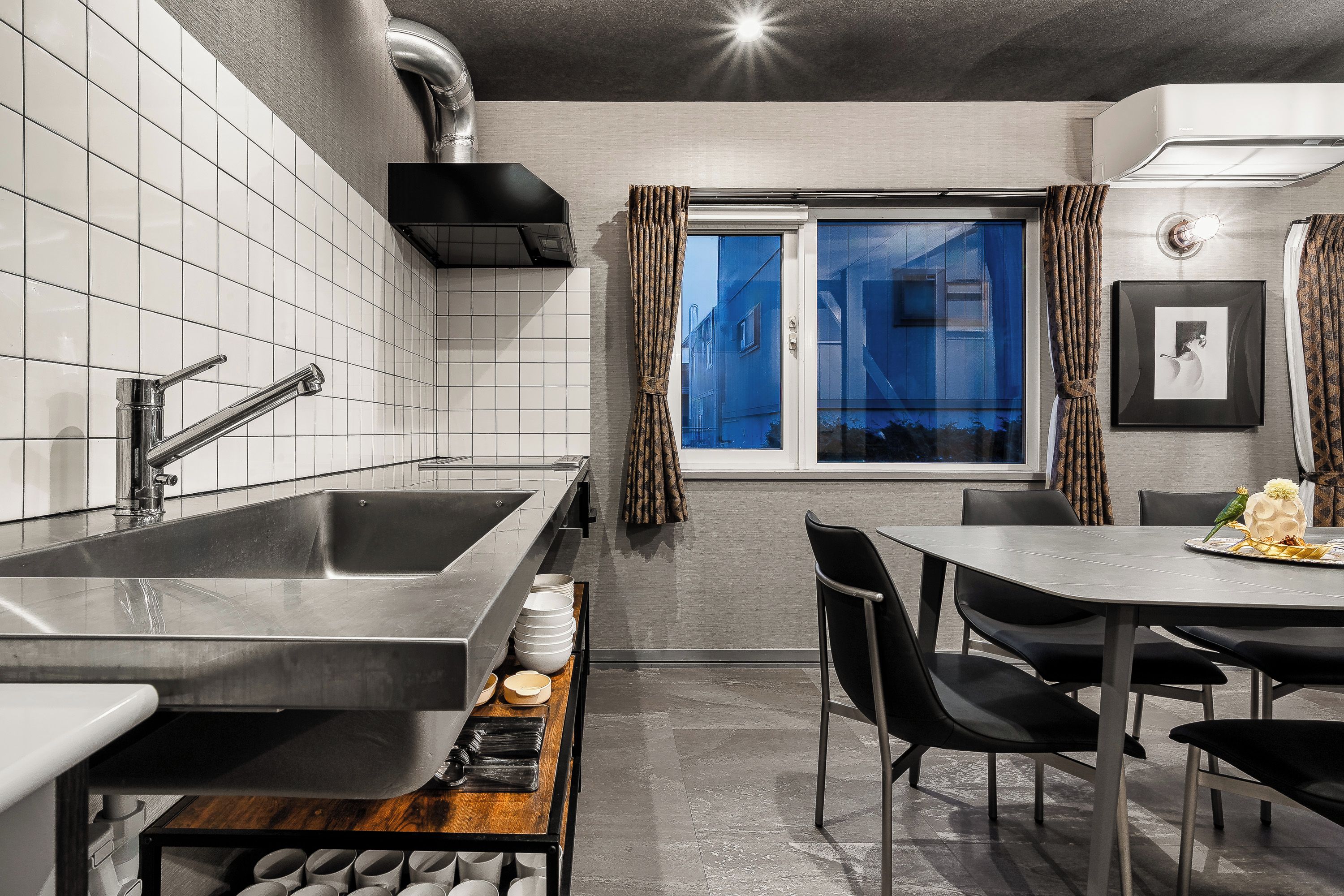 A modern kitchen with a large sink, a dining area with a table and chairs, and a window with curtains.