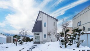 A modern two-story house with a sloped roof, a front entrance, and a snow-covered yard. - THE LAVENRIDGE (Nakafurano)