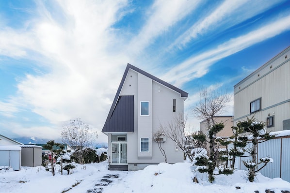 A modern two-story house with a sloped roof, a front entrance, and a snow-covered yard.