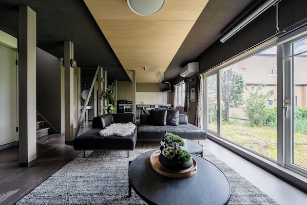 A modern living room with a sofa, a coffee table with a plant, and a view of the outdoors through large windows.