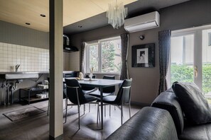 A modern kitchen with a dining area, including a table with chairs, a sofa, and a view of the outdoors. - THE LAVENRIDGE (Nakafurano)