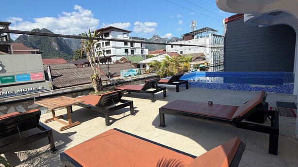 A rooftop lounge with sun loungers and a pool area, overlooking a mountainous landscape and residential buildings. - VangVieng Boutique Hotel (Vang Vieng)