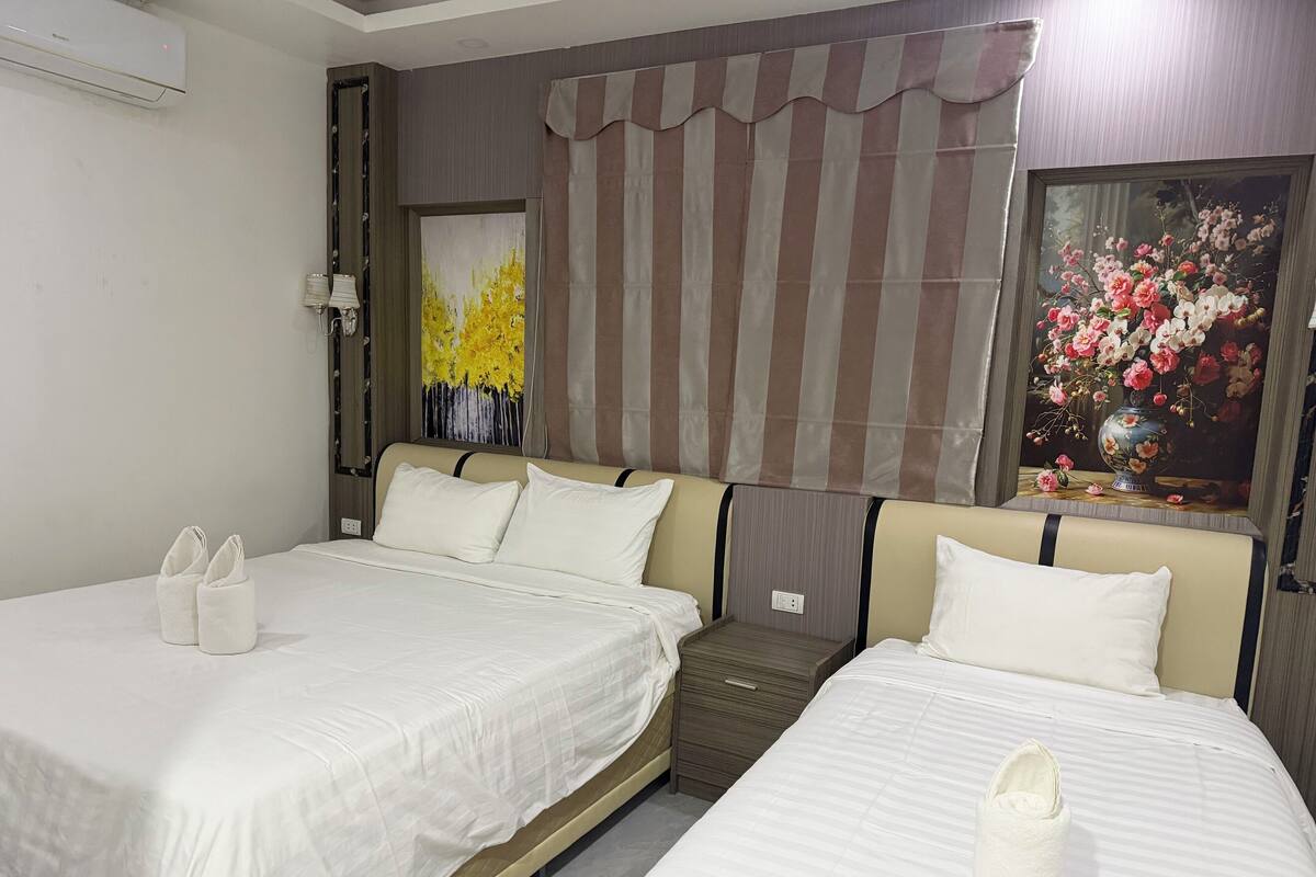 A hotel room with two beds, a painting of flowers, a striped curtain, and a bedside table.