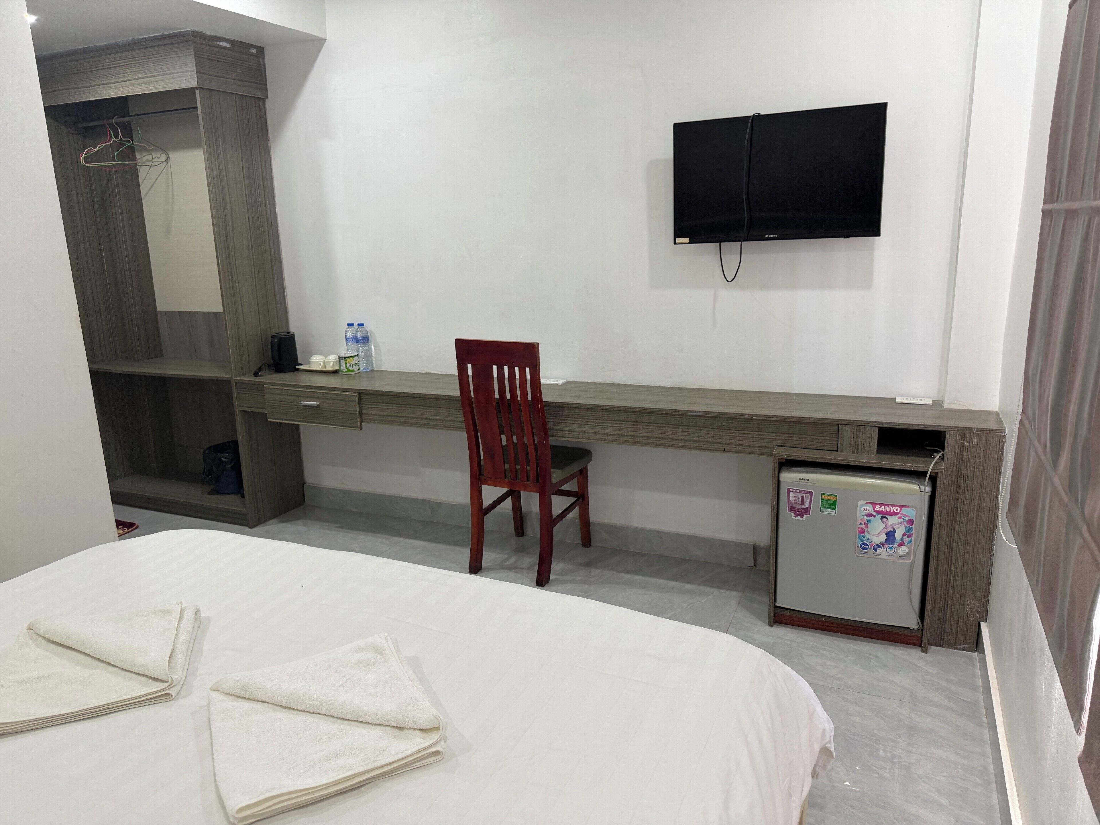 A hotel room with a bed, a desk, a chair, a TV, and a mini-fridge.