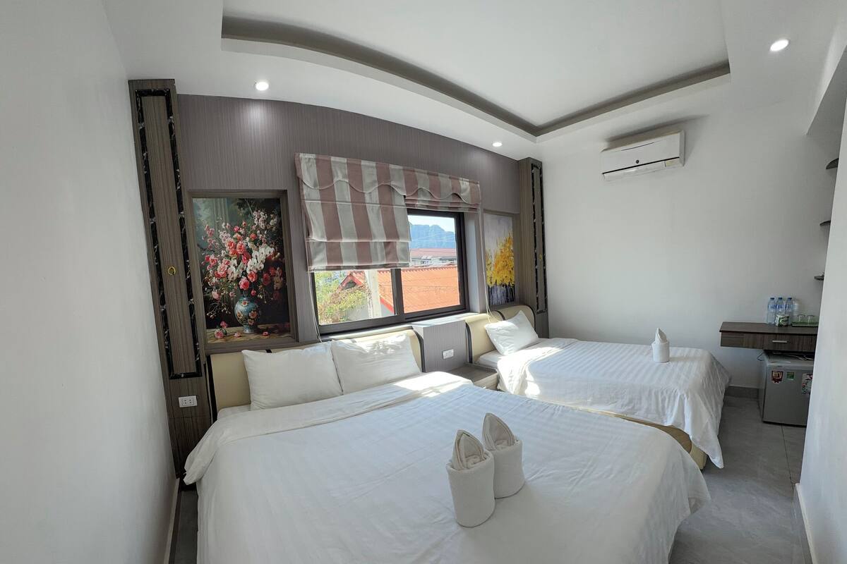 A hotel room with two beds, a small desk, and a window with a view of the outside.