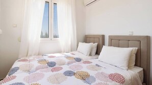 A bedroom with a bed, white curtains, an air conditioning unit, and a window with a view. - Villa Phoebe Gennadi (2W76+JJ South Rhodes, Greece)