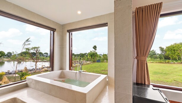 A modern bathroom with a large bathtub, a view of a lake, and a well-maintained garden. - Cuc Phuong Tropical Retreat (Phu Long)