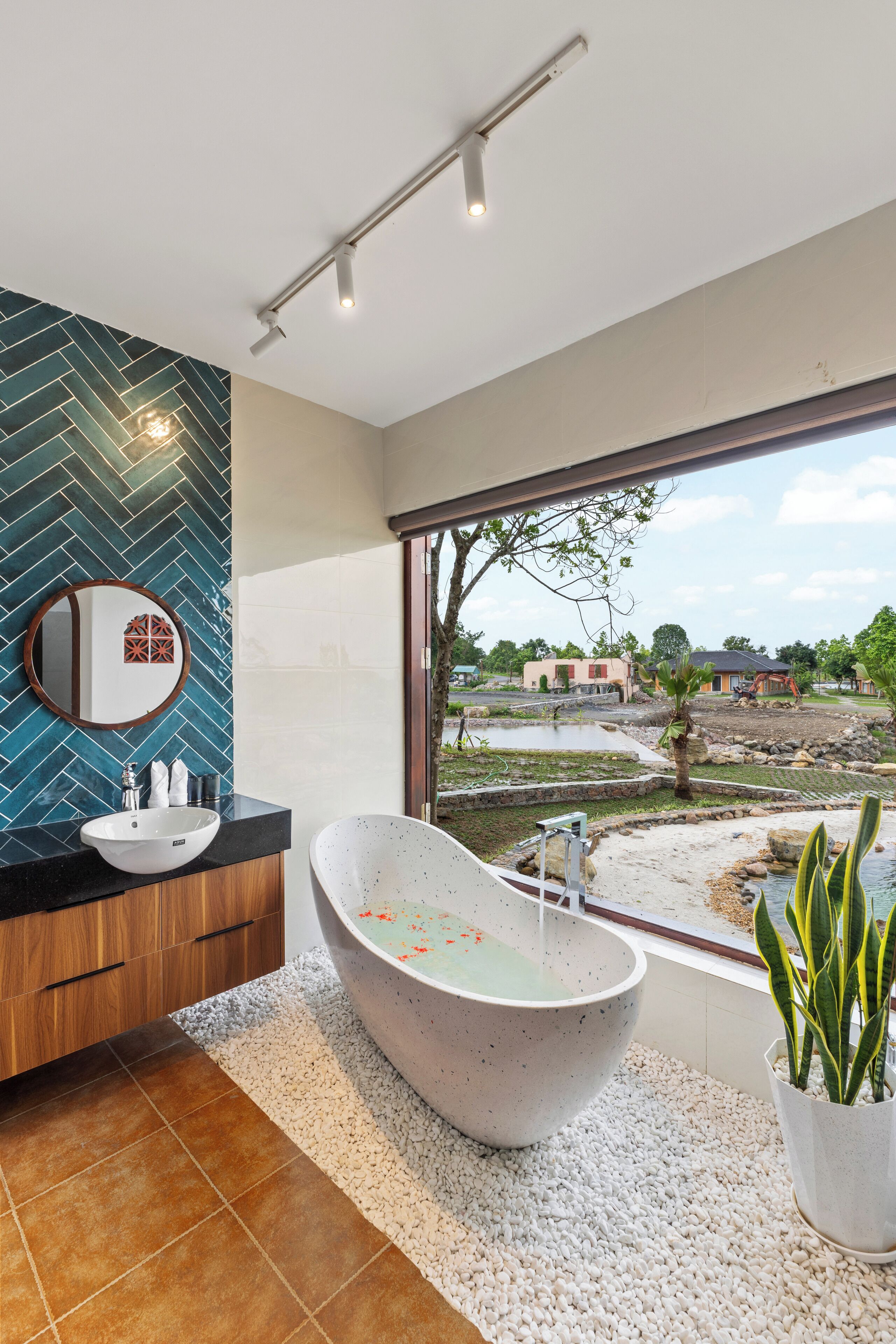 Un baño moderno con una bañera independiente, un espejo redondo y vistas a una obra en construcción a través de un ventanal grande.
