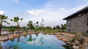 A stone building with a tiled roof, a pond with rocks, and palm trees. - Cuc Phuong Tropical Retreat (Phu Long)