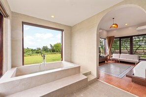 Un bagno moderno con una grande vasca, vista sull'esterno e una zona relax con divano e tappeto.