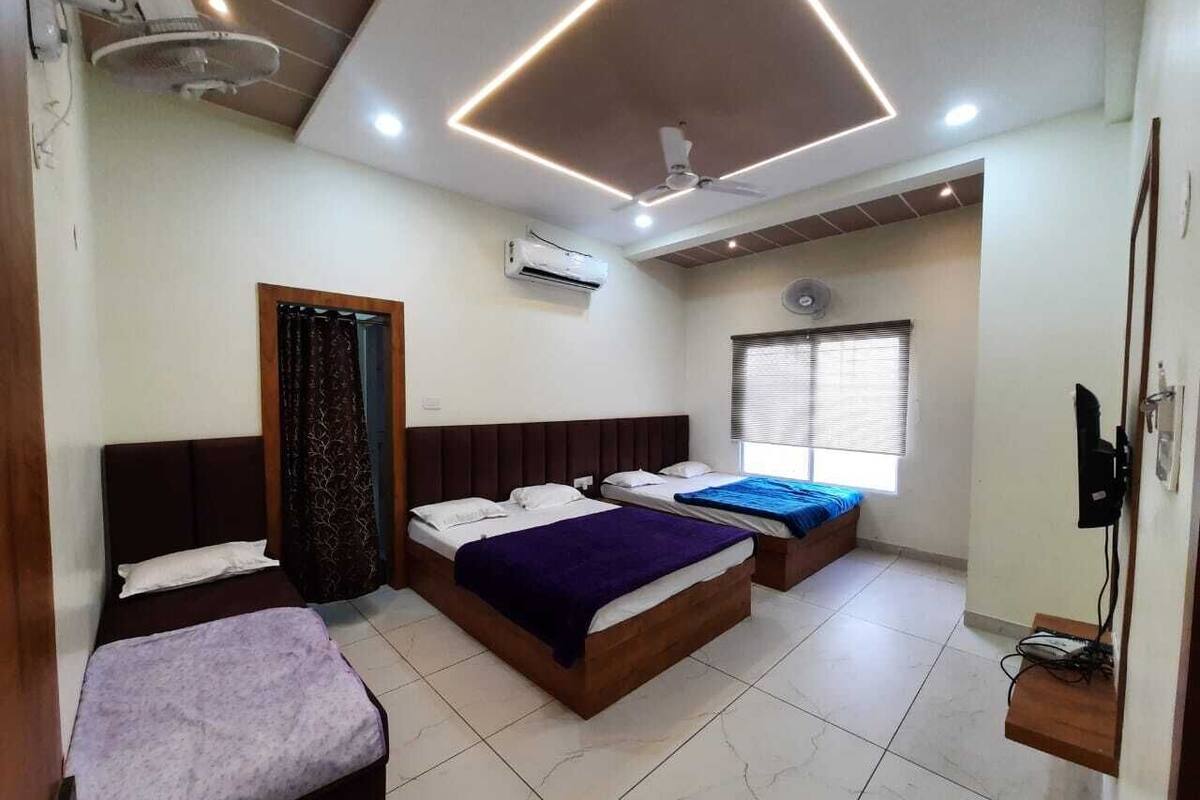 Una habitación con tres camas, ventilador de techo, aire acondicionado y ventana con persianas.