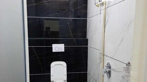 Une petite salle de bain avec des toilettes, un seau et une baignoire.