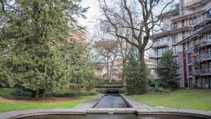 A tranquil courtyard with a central water feature, surrounded by mature trees and adjacent multi-story residential buildings. - Brussels EU Center residence (Brussels)