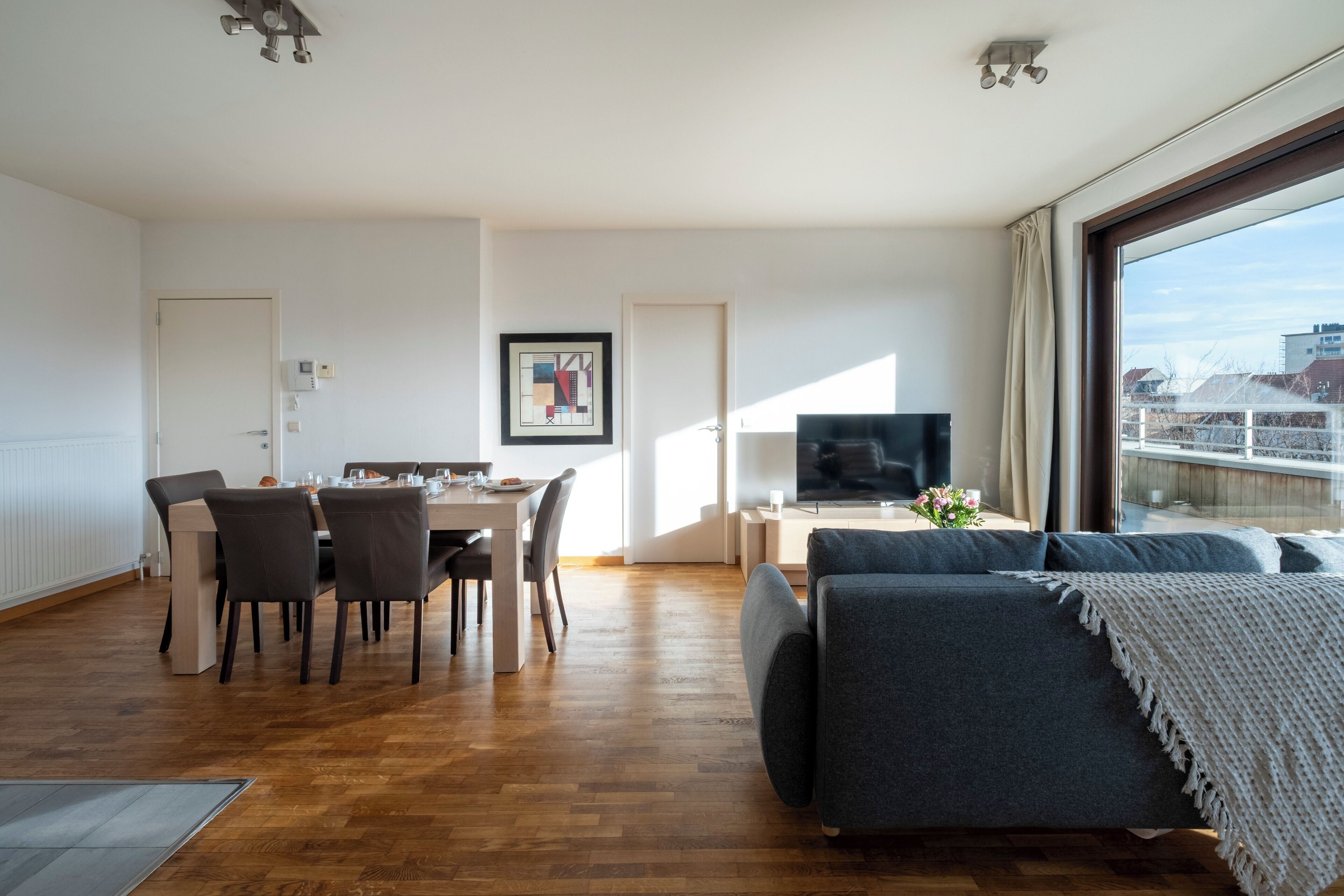 A modern living room with a dining area, a sofa, and a TV.
