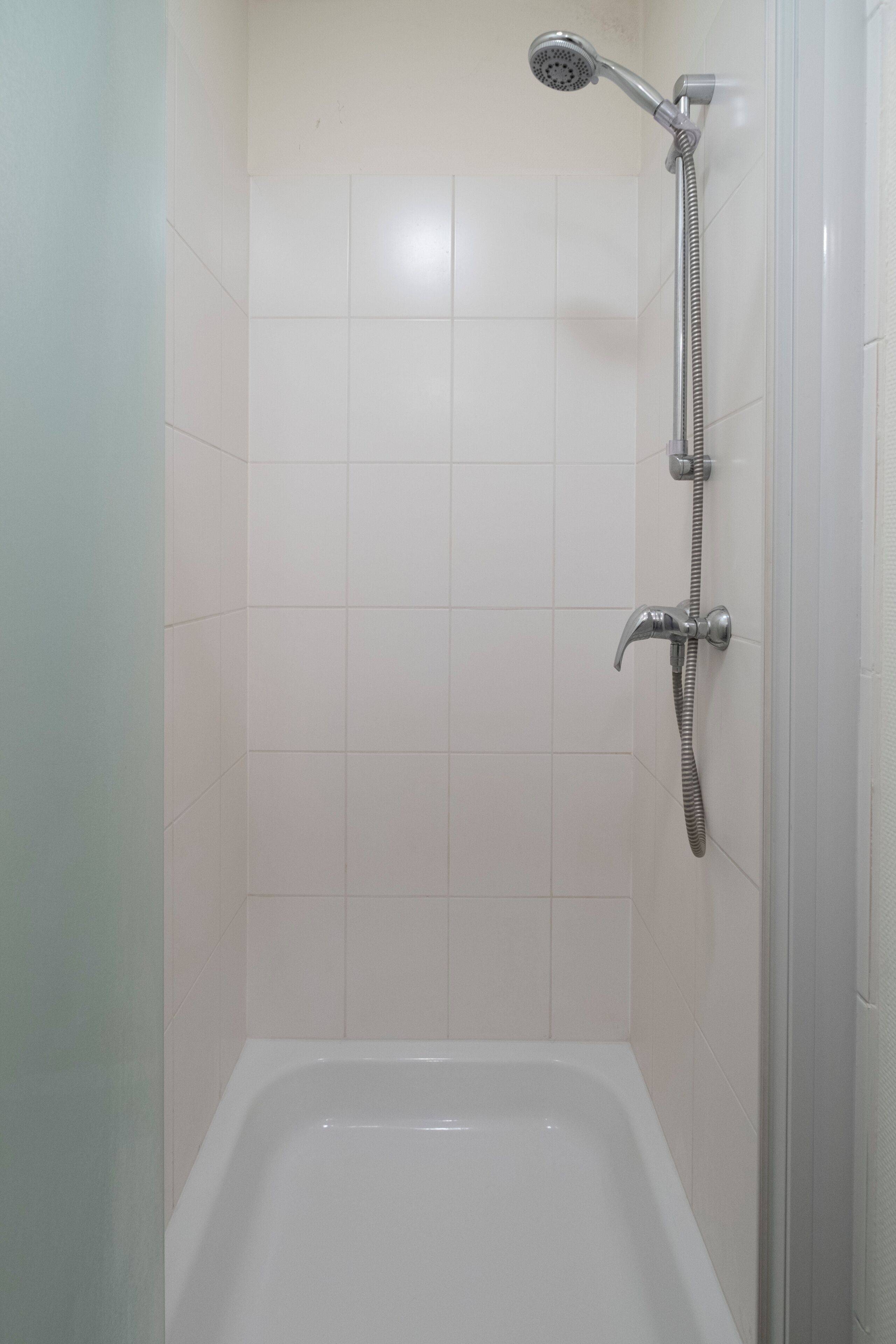 Une salle de bain avec une douche, une baignoire et des murs recouverts de carreaux blancs.