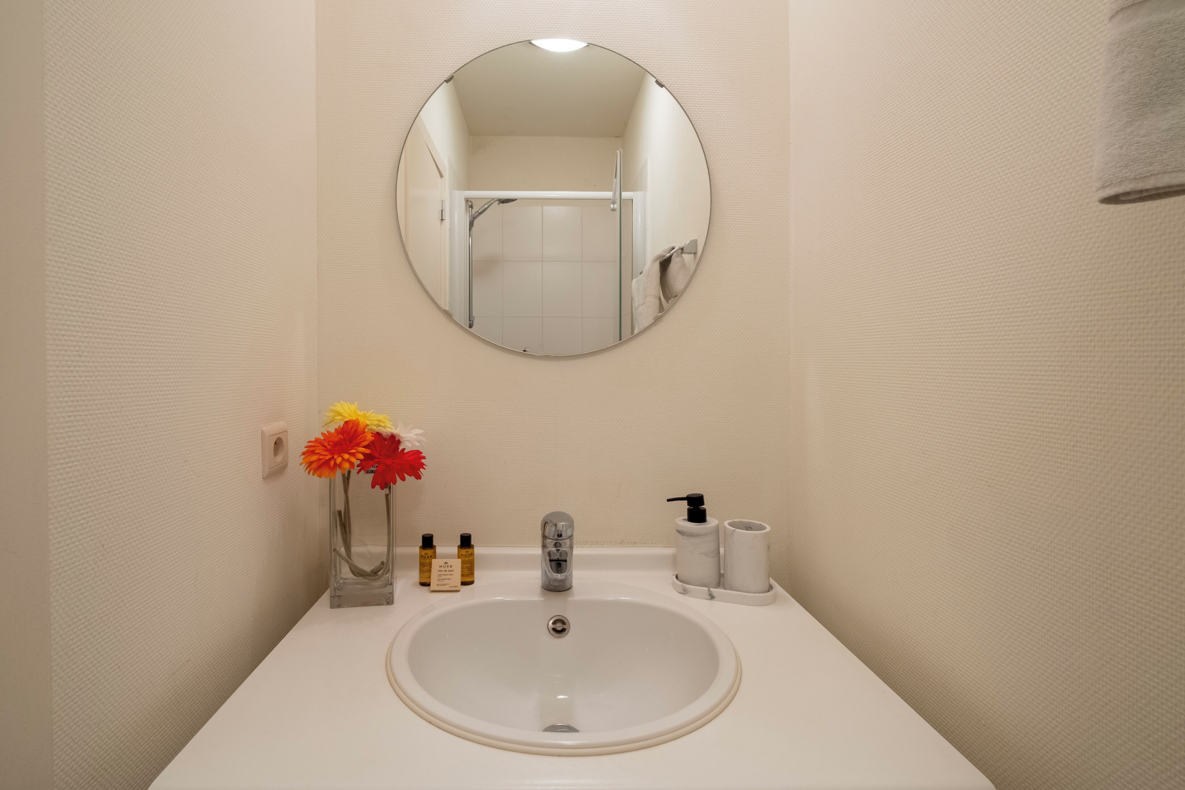 A bathroom with a round mirror, a white sink, and toiletries.