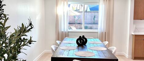 Un coin repas avec une table en bois, des chaises blanches et un vase noir servant de centre de table.