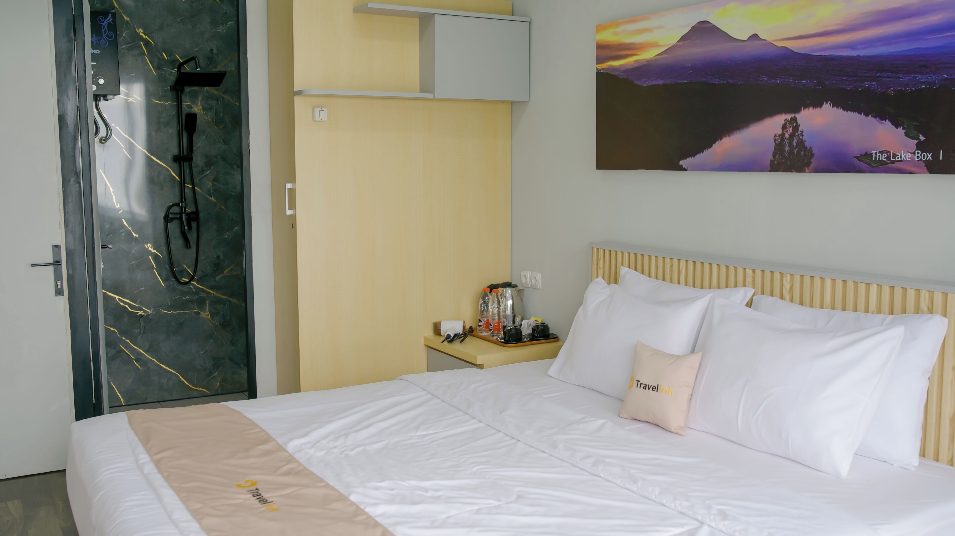 A hotel room with a bed, a nightstand, a painting, and a bathroom with a mirror and towel rack.
