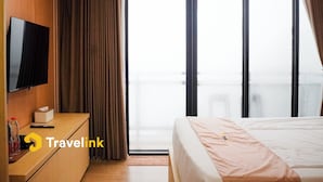 A hotel room with a bed, a TV on a wooden dresser, a window with curtains, and a view of the city.