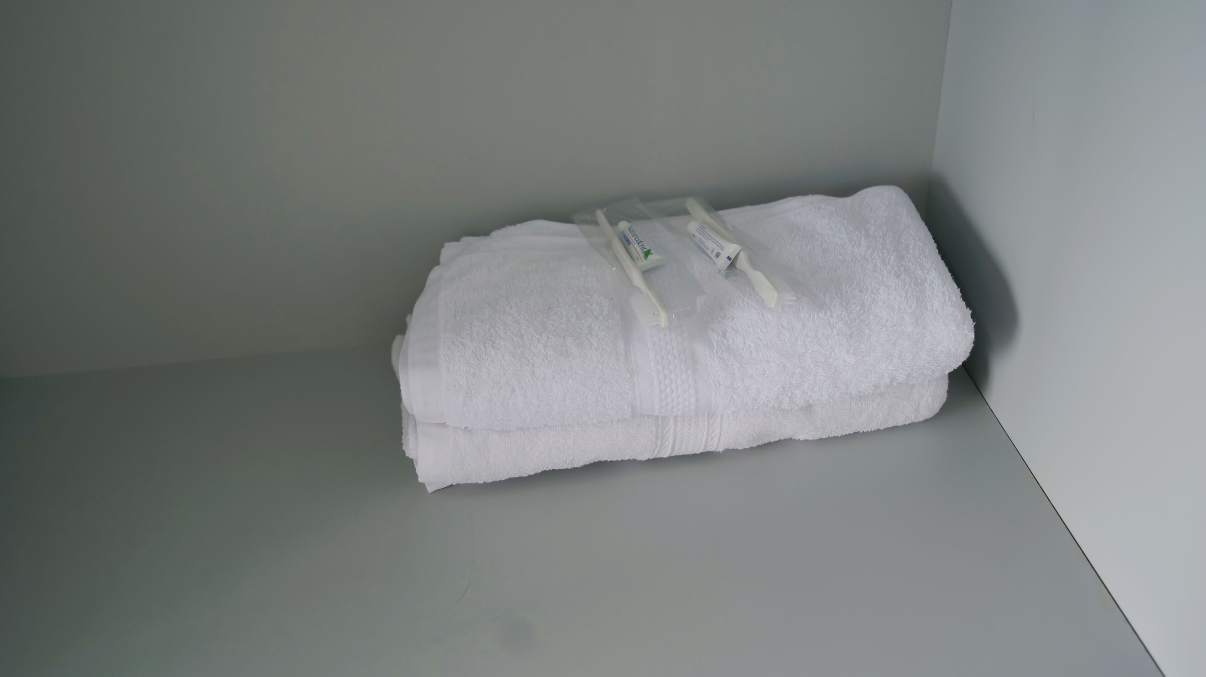 Toalha branca dobrada cuidadosamente sobre uma superfície branca em um quarto com paredes lisas.