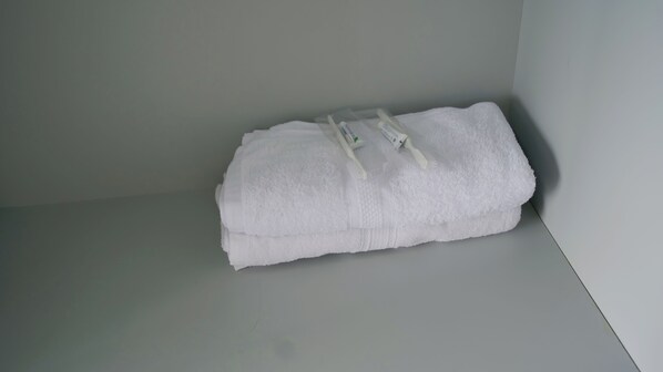 A neatly folded white towel on a white surface in a room with plain walls. - The Lakebox Menjer by Travelink (Garung)