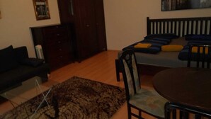 A room with a dark wooden wardrobe, a bed with blue and orange pillows, a small round table, and a dark-colored sofa. - Chic 1BR Flat in Heart of Vienna (Vienna)